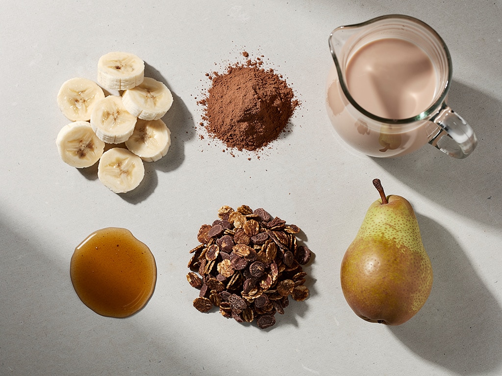 Zutaten für die Smoothie-Bowl mit Bananenscheiben, Kakao, Mandeldrink und Birne